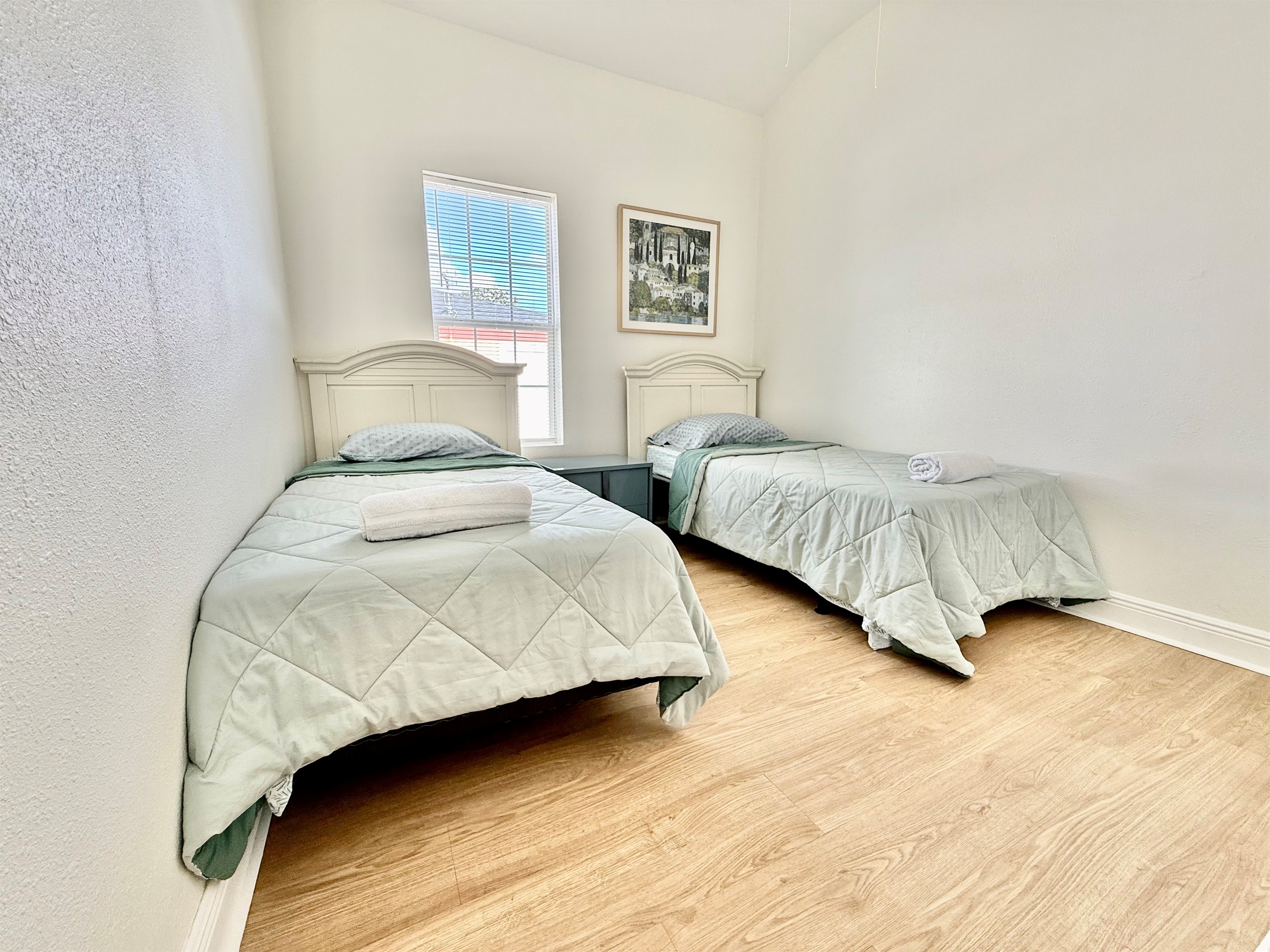 A cheerful and functional setup with twin beds, light wood flooring, and a window view to let in morning sunshine.