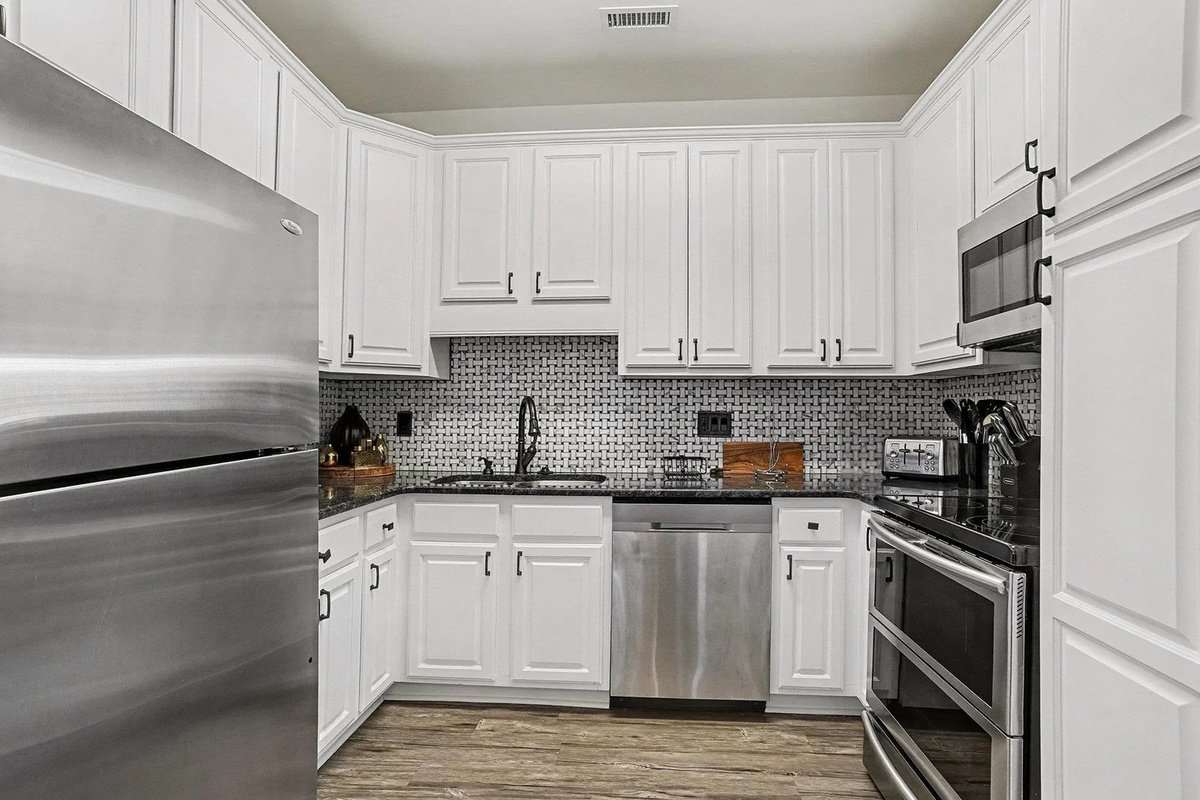 Bright white kitchen with granite counters, dishwasher, and stainless steel appliances