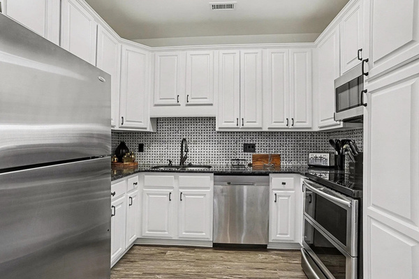 Bright white kitchen with granite counters, dishwasher, and stainless steel appliances