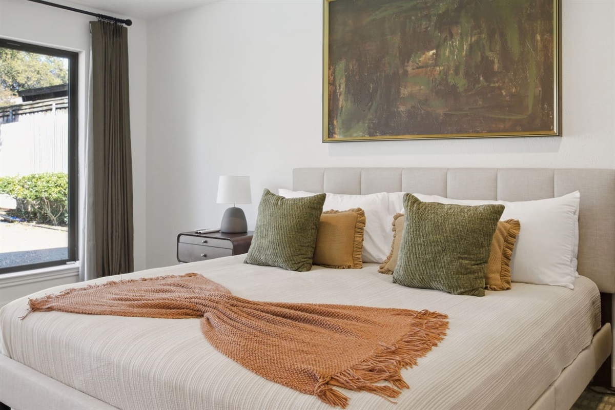 Luxe primary bedroom with a king bed, 65” Smart TV, cozy sitting area, full-length mirror, and ceiling fan for added comfort.