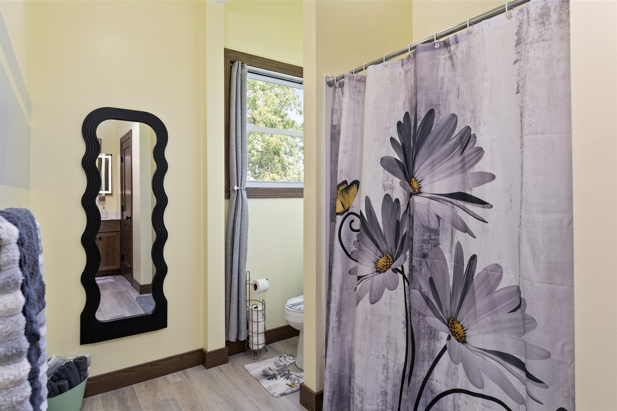 Bright and cheerful bathroom featuring modern décor, floral accents, and a unique wavy mirror for added charm. Main floor