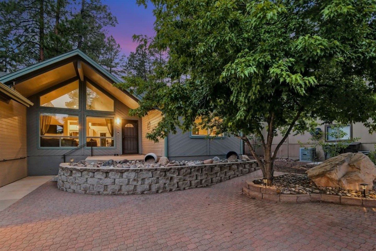 Evening courtyard view with mature trees, patio space, and warm interior lighting.