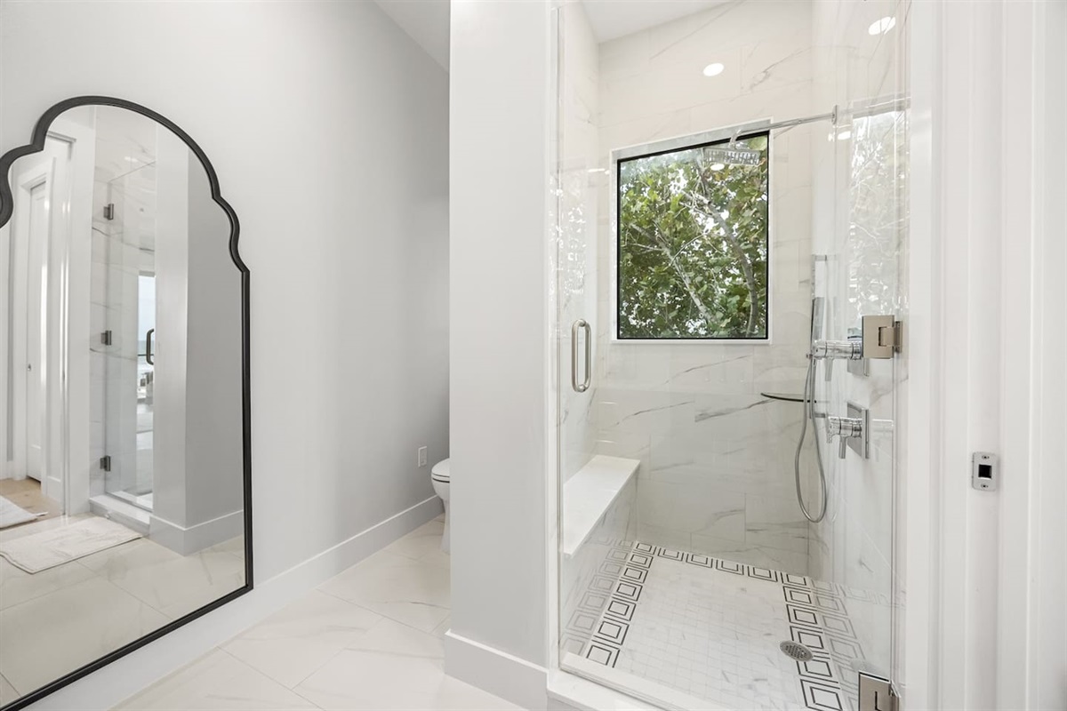 Experience luxury in this bathroom with an elegant shower featuring a sleek glass cover, a toilet nearby, beautiful flooring tiles, and a full-body mirror adding a touch of sophistication.