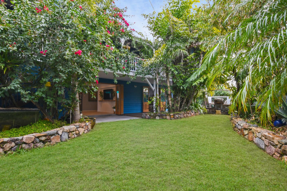 Dense palms, flowering greenery and stone-edged garden beds give the backyard at Aaron's Beachside Boat House a private, tropical hideaway feel.