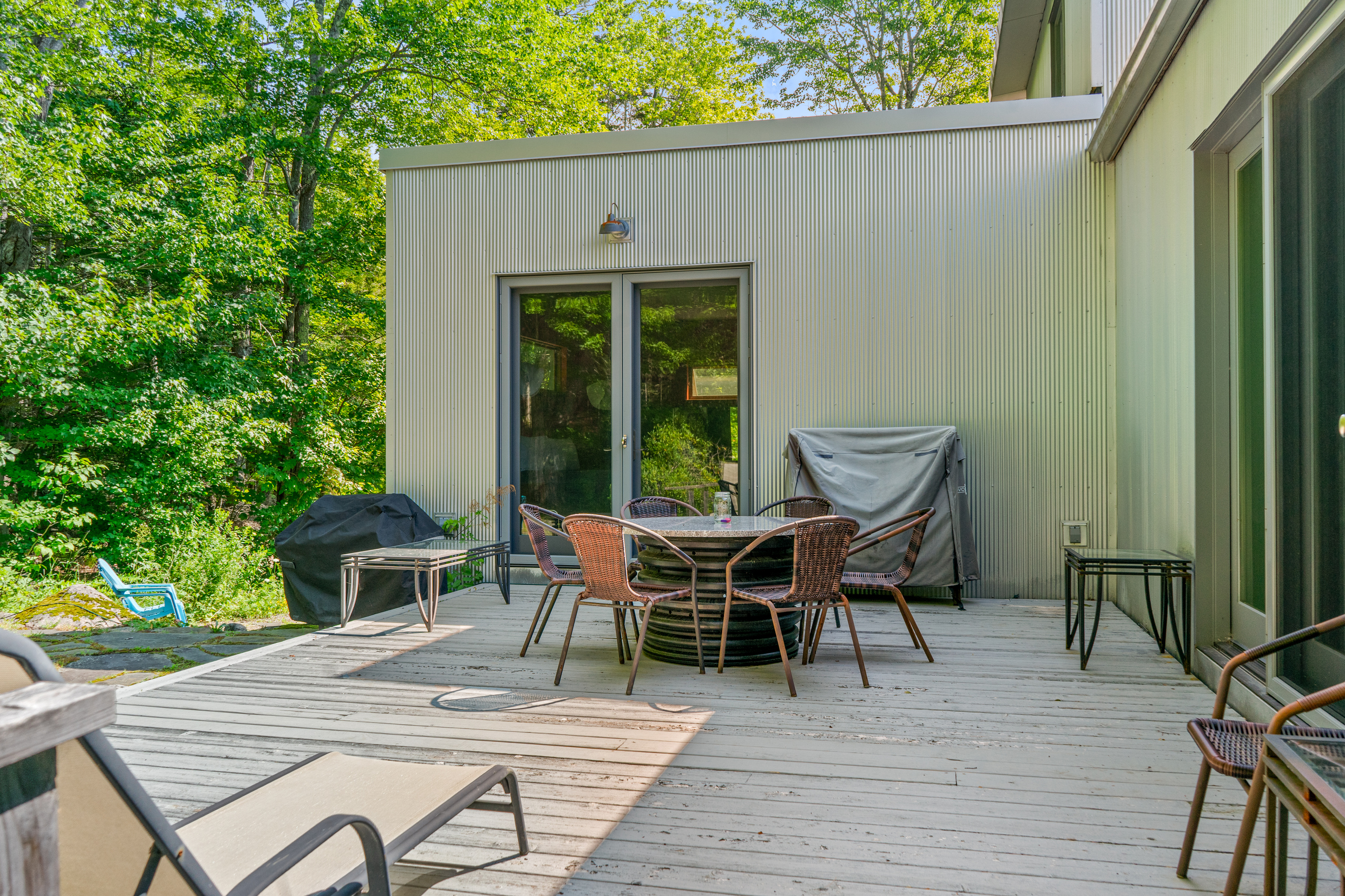 The main outdoor living space at "The Crag." This spacious deck features a circular dining setup, sun lounger, covered grill, and direct access to both the primary suite and main lounge—all bordering Acadia National Park.