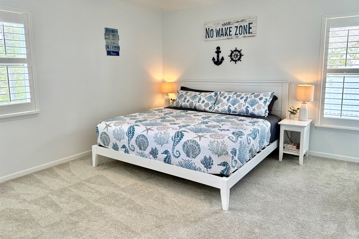 Spacious king suite with soft carpet, coastal décor, and plenty of natural light — your private retreat.