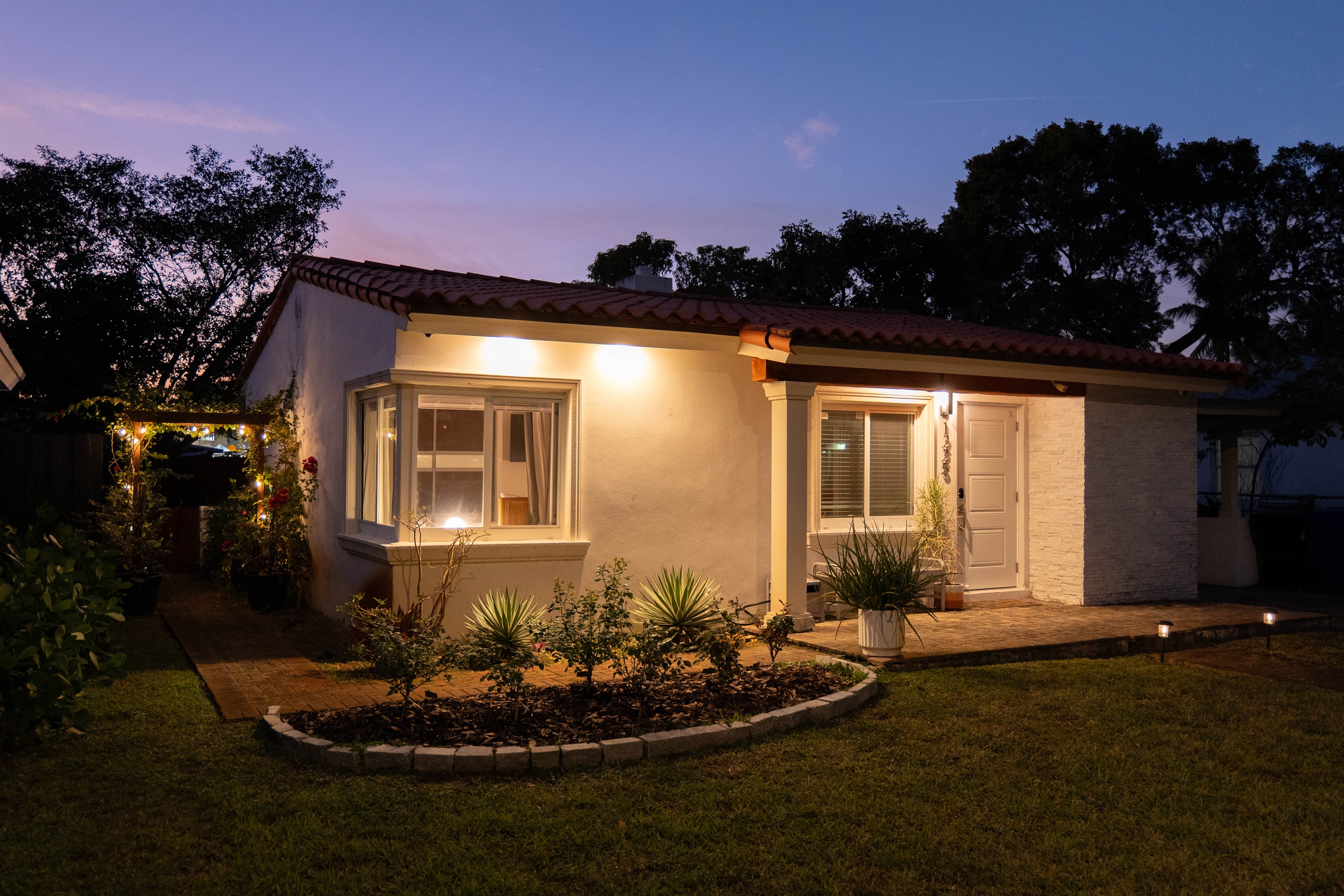 Front view of the home illuminated by exterior lighting with landscaped garden beds