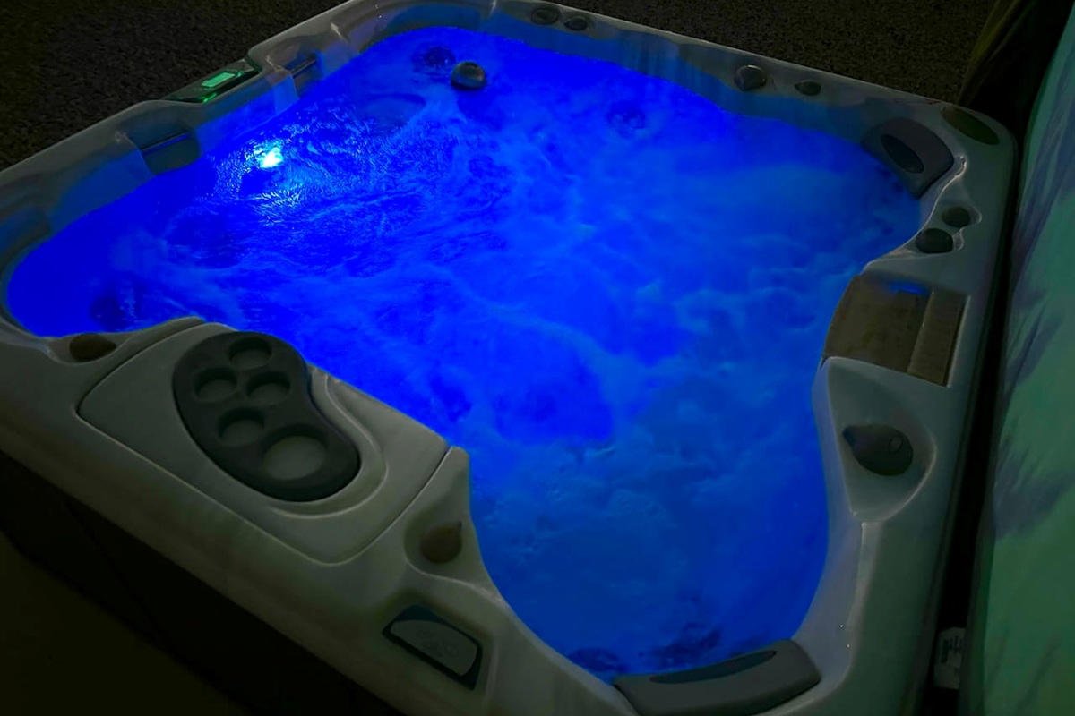 Set the mood for a relaxing evening with the vibrant LED lighting in this private backyard hot tub. The glowing blue water and powerful jets create a peaceful atmosphere for unwinding under the stars after a long day.