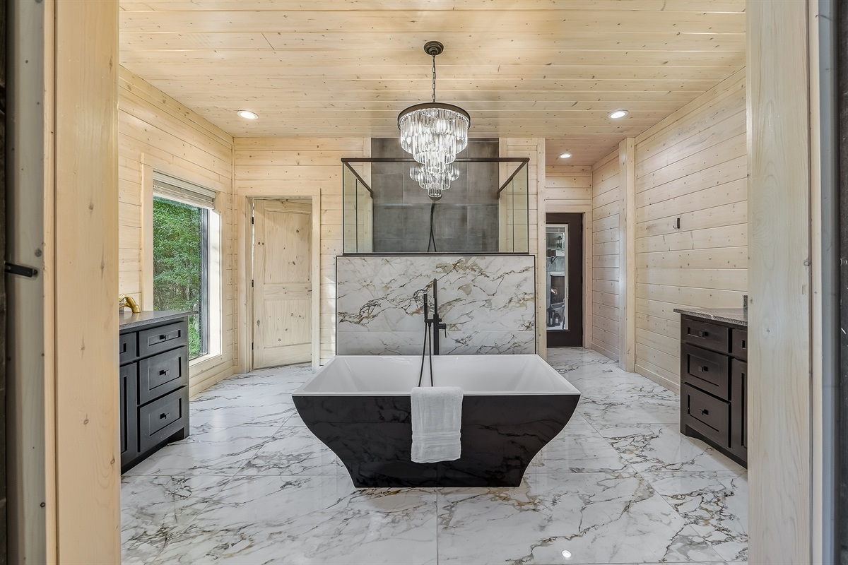 Spa level bathroom with marble inspired tile, chandelier lighting, and a deep soaking tub for total relaxation.