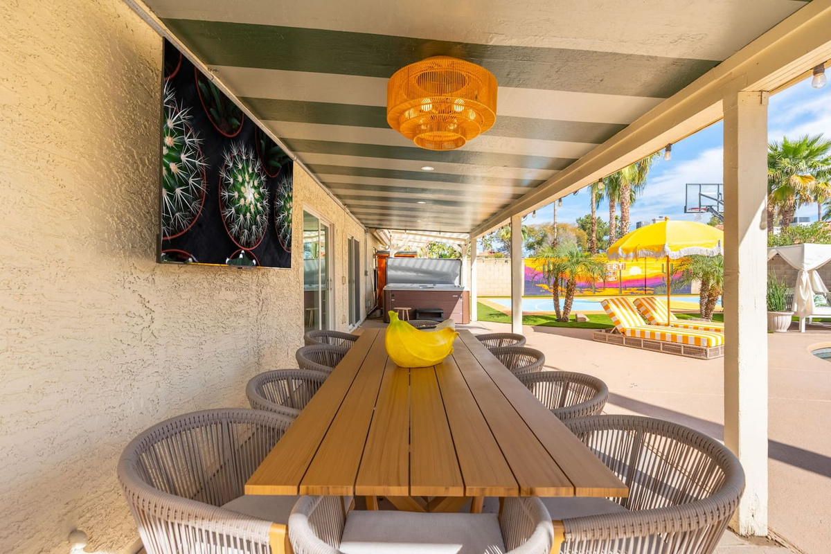 Covered outdoor dining with striped ceiling, long wooden table, and pool views—perfect for al fresco meals and entertaining.