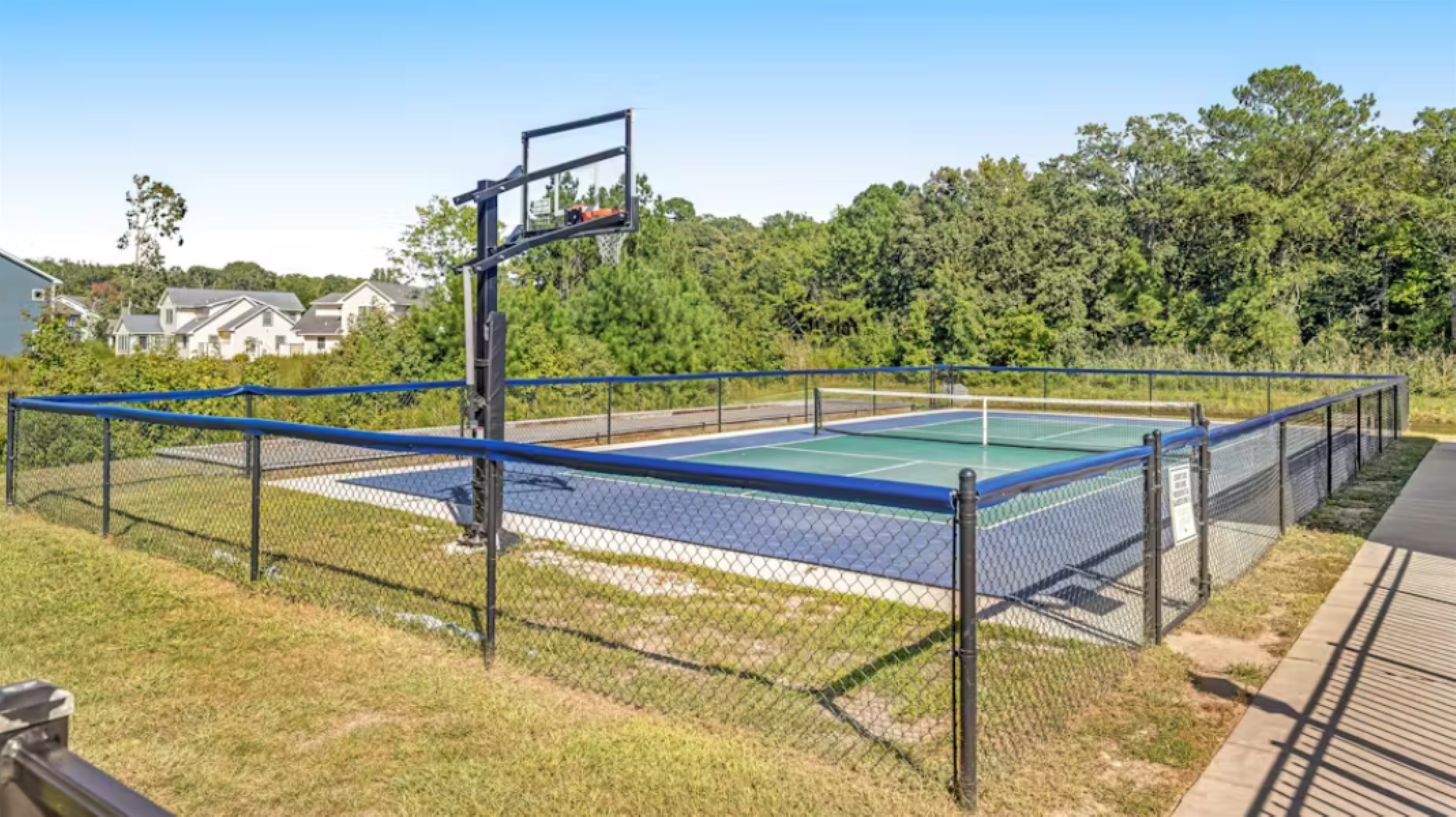 Versatile sports court with a regulation basketball hoop and tennis/pickleball lines, fully fenced for safe, active fun.
