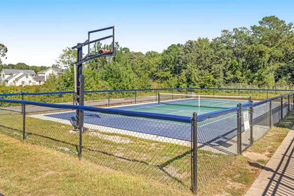 Versatile sports court with a regulation basketball hoop and tennis/pickleball lines, fully fenced for safe, active fun.