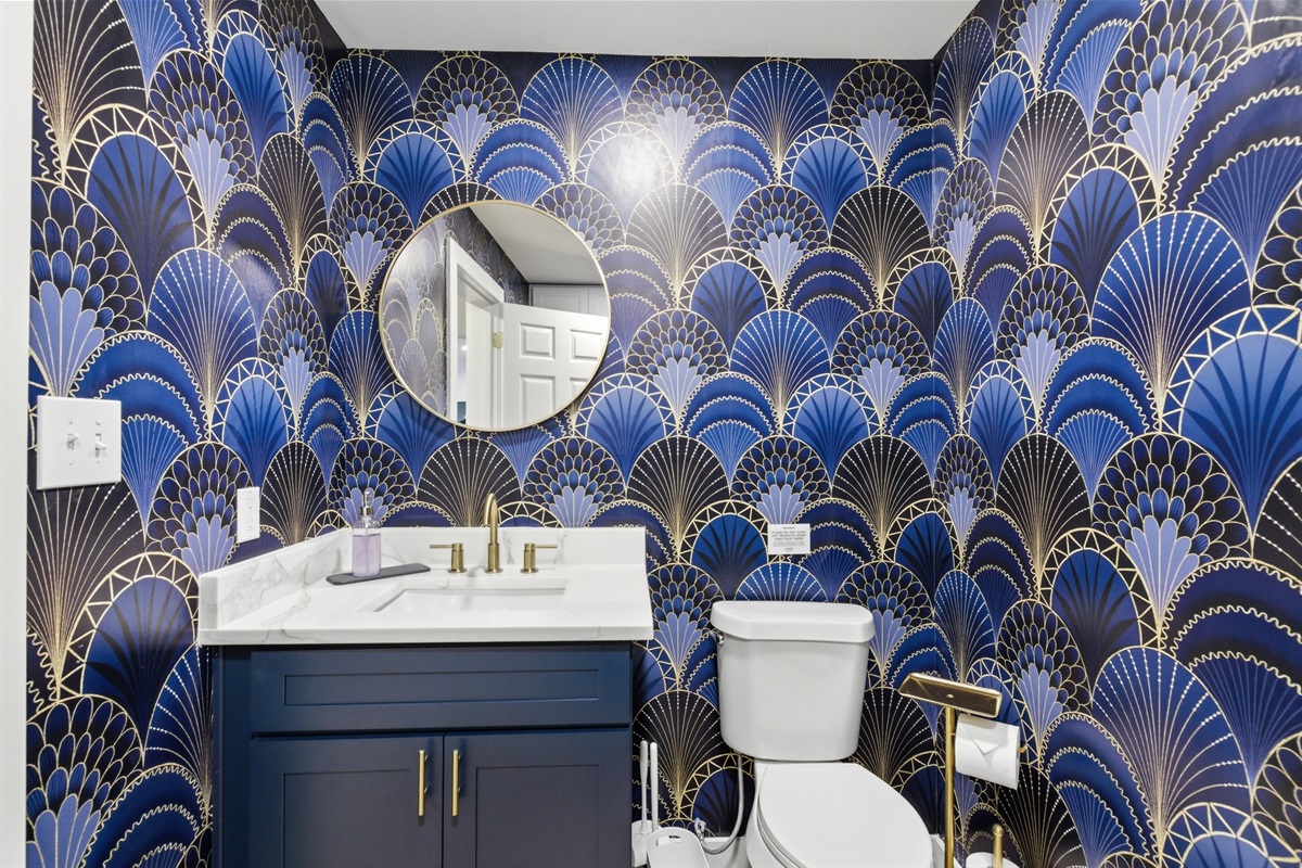 Bold art deco half bath with navy and gold vanity, statement wallpaper, and round mirror. Stocked with Ginger Lily Farms essentials. Steps from AT&T Stadium, Arlington TX.