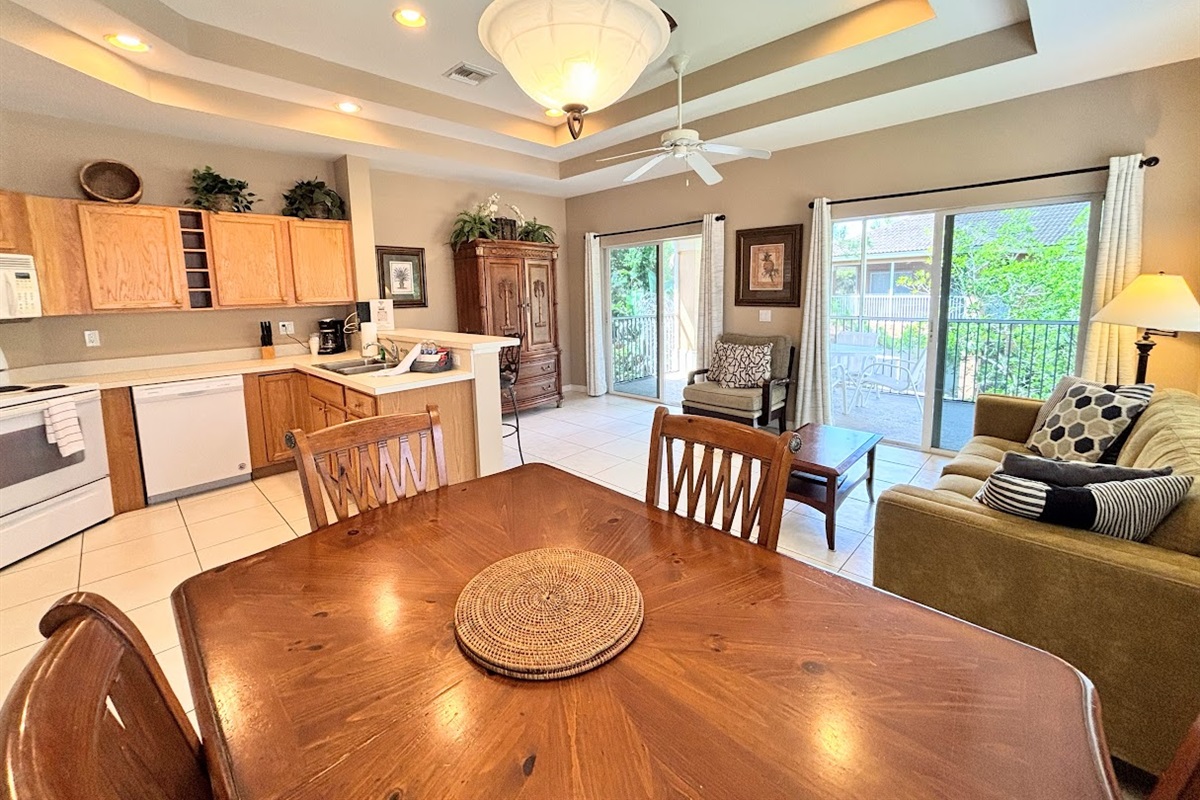 Bright and spacious open-concept living area featuring vaulted tray ceilings, a fully equipped kitchen, comfortable seating, and sliding glass doors leading out to a private screened balcony.