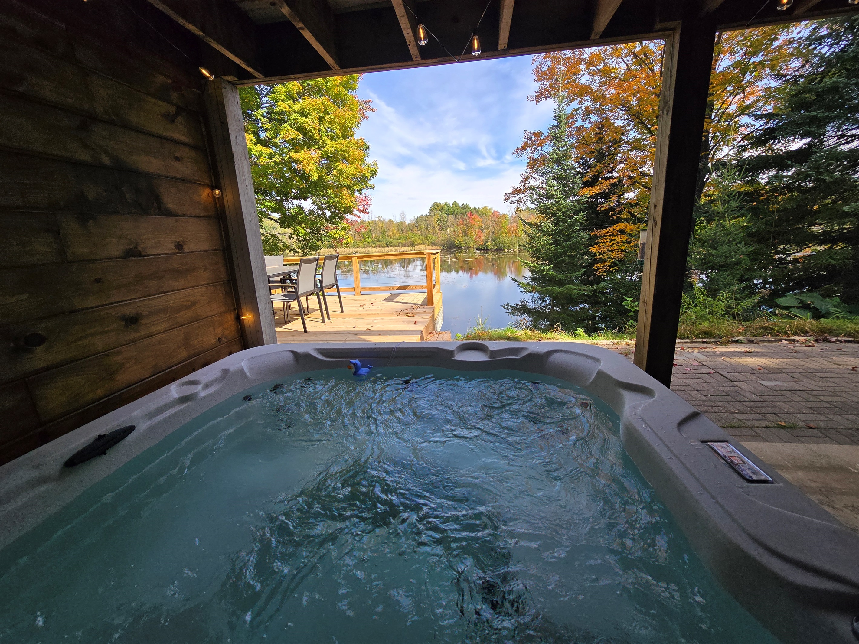 Unwind in our covered lakeside hot tub with stunning views! ✨ Enjoy bubbling water, peaceful nature, and vibrant trees—perfect for sunrise coffee or a relaxing sunset soak. 🌲🌅