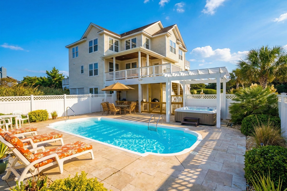 A view of the home's rear exterior showcasing the multi-level decks and the sparkling private pool area surrounded by a white privacy fence.
