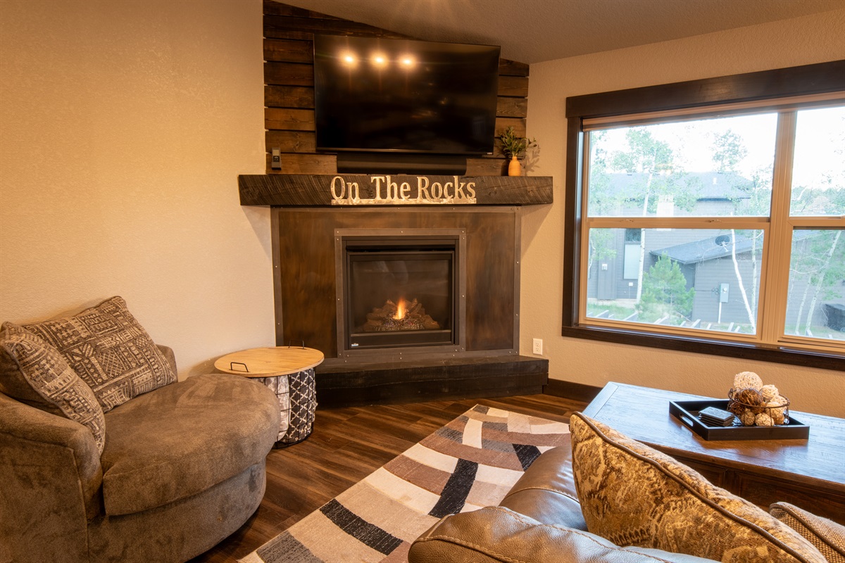 Imagine relaxing in the welcoming living room at "On The Rocks," where the fireplace's gentle fire creates a cozy ambiance.