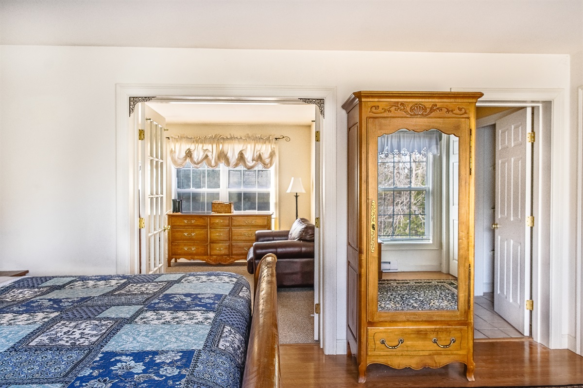 The Primary Suite includes a private sitting room separated by elegant French doors. This quiet annex features a leather loveseat and a large dresser, providing an intimate spot for morning coffee or a peaceful evening on the "Quiet Side."