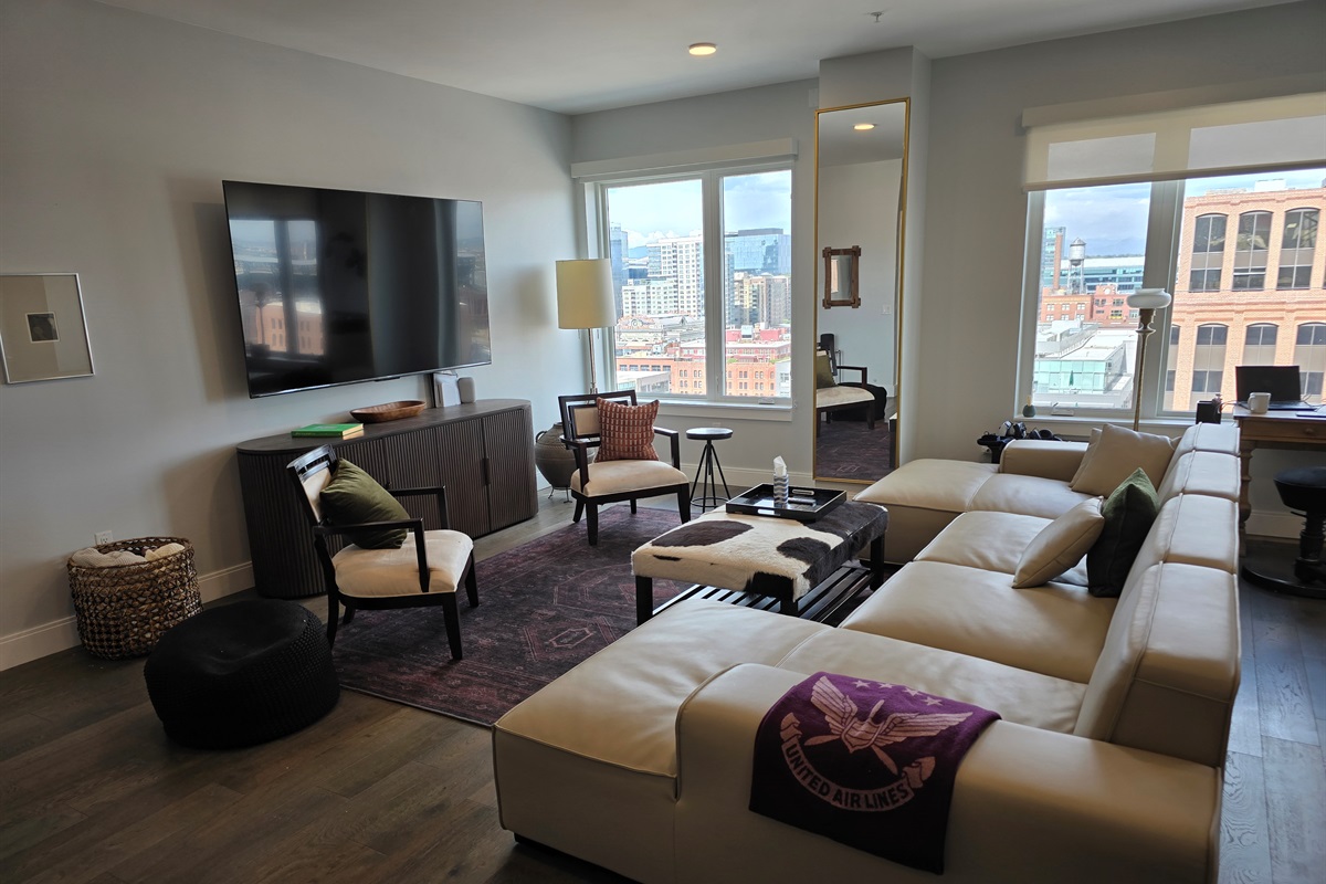 ✨ Spacious living room with designer sectional, 85" Smart TV, and skyline views.