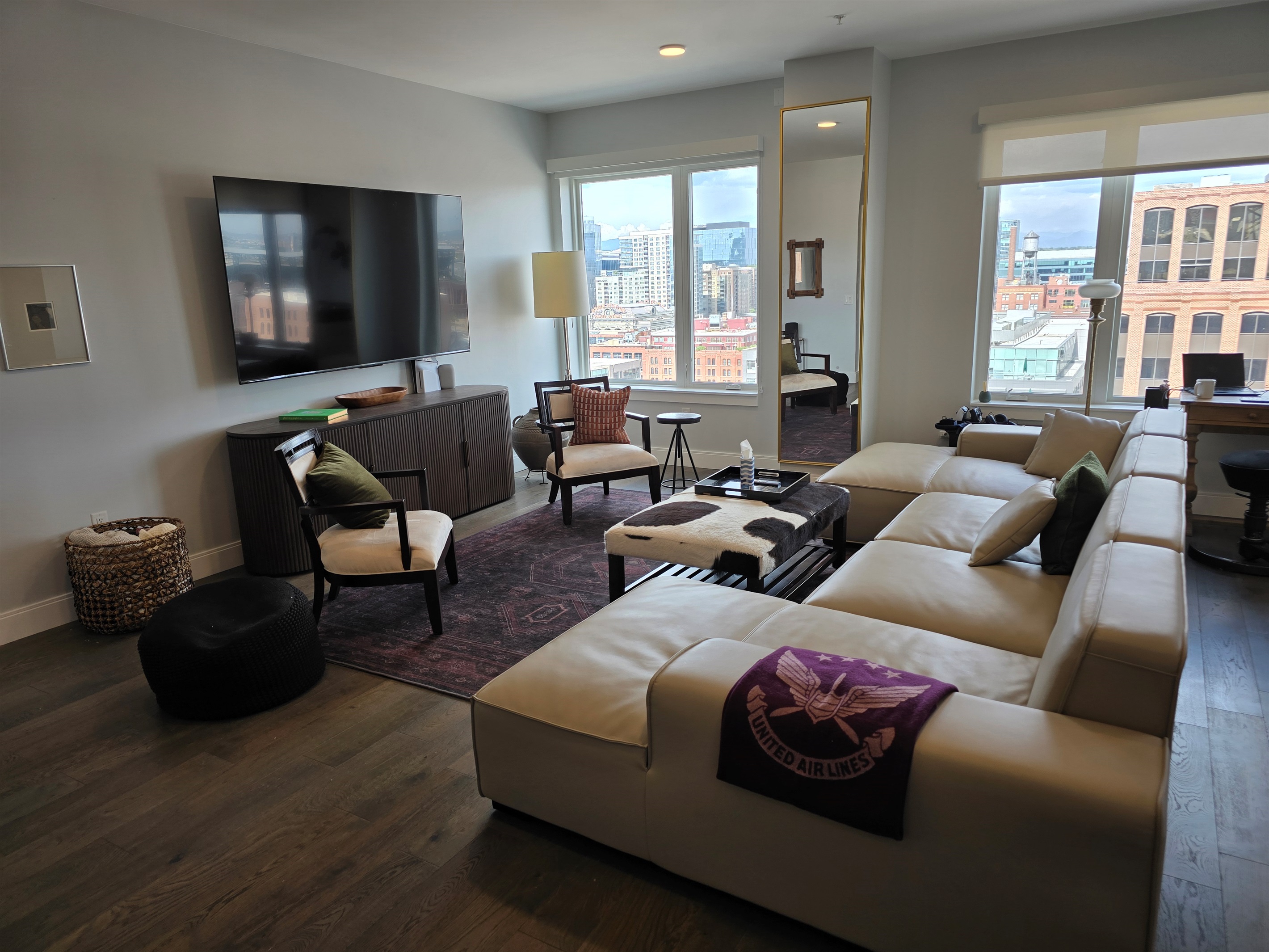 ✨ Spacious living room with designer sectional, 85" Smart TV, and skyline views.