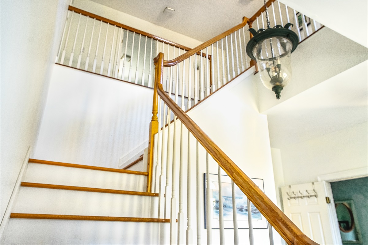 Ascend the elegant turning staircase to the second-floor sleeping quarters. Featuring a striking hanging light fixture and bright, airy design, this grand entry leads to the private retreats of Seven Peaks Ridge near Acadia National Park.