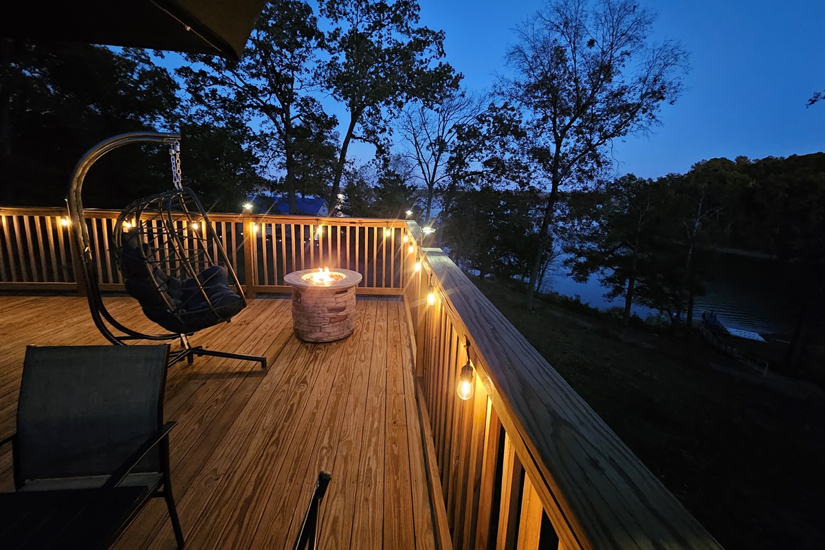 Peaceful lakeview deck at dusk — cozy fire pit, ambient lighting, and hanging chair for unforgettable evenings