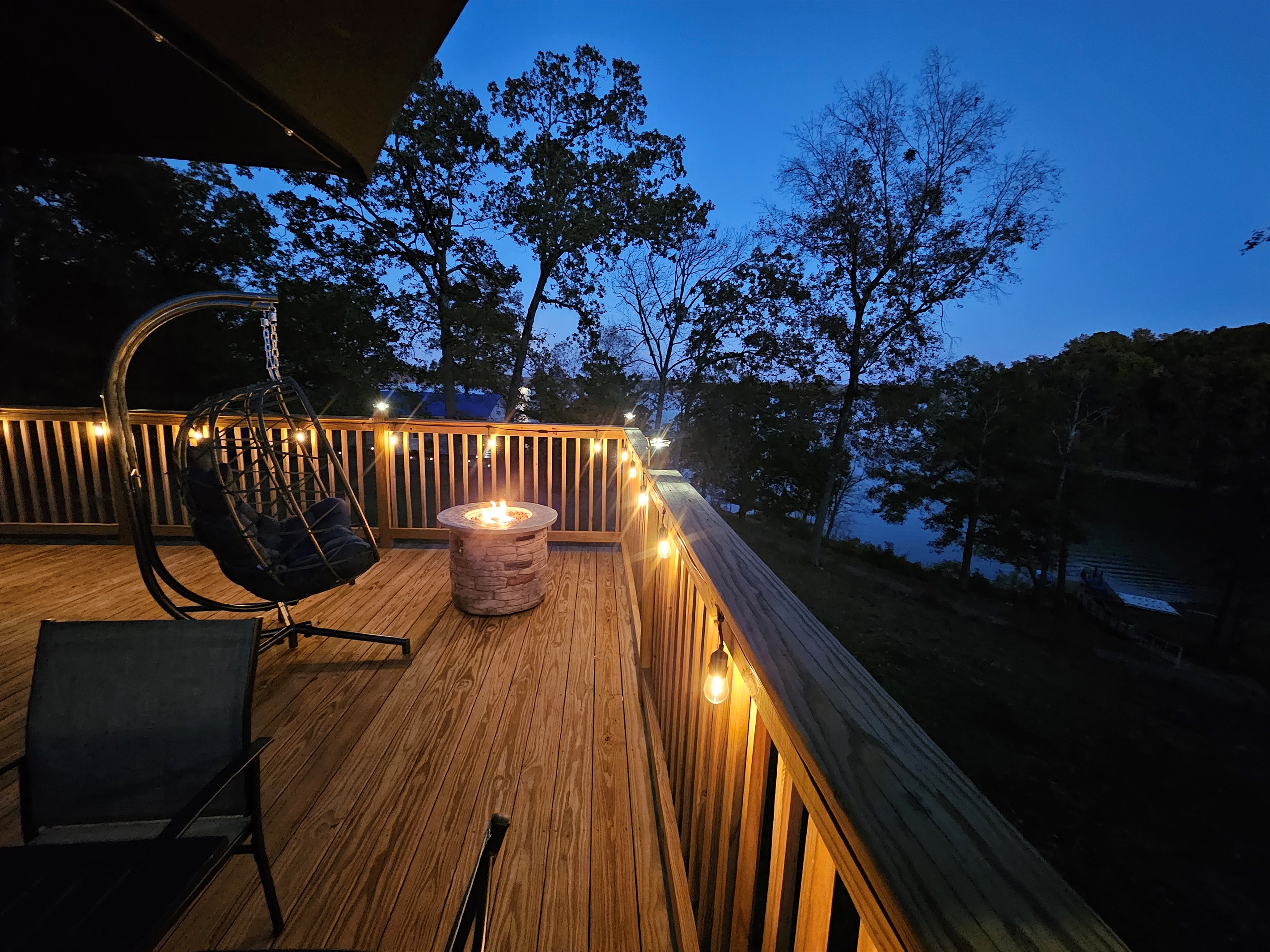 Peaceful lakeview deck at dusk — cozy fire pit, ambient lighting, and hanging chair for unforgettable evenings