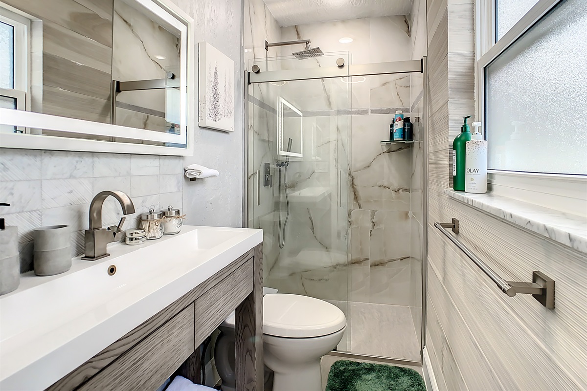 Modern bathroom with glass-enclosed shower, vanity, and large window for natural light.
