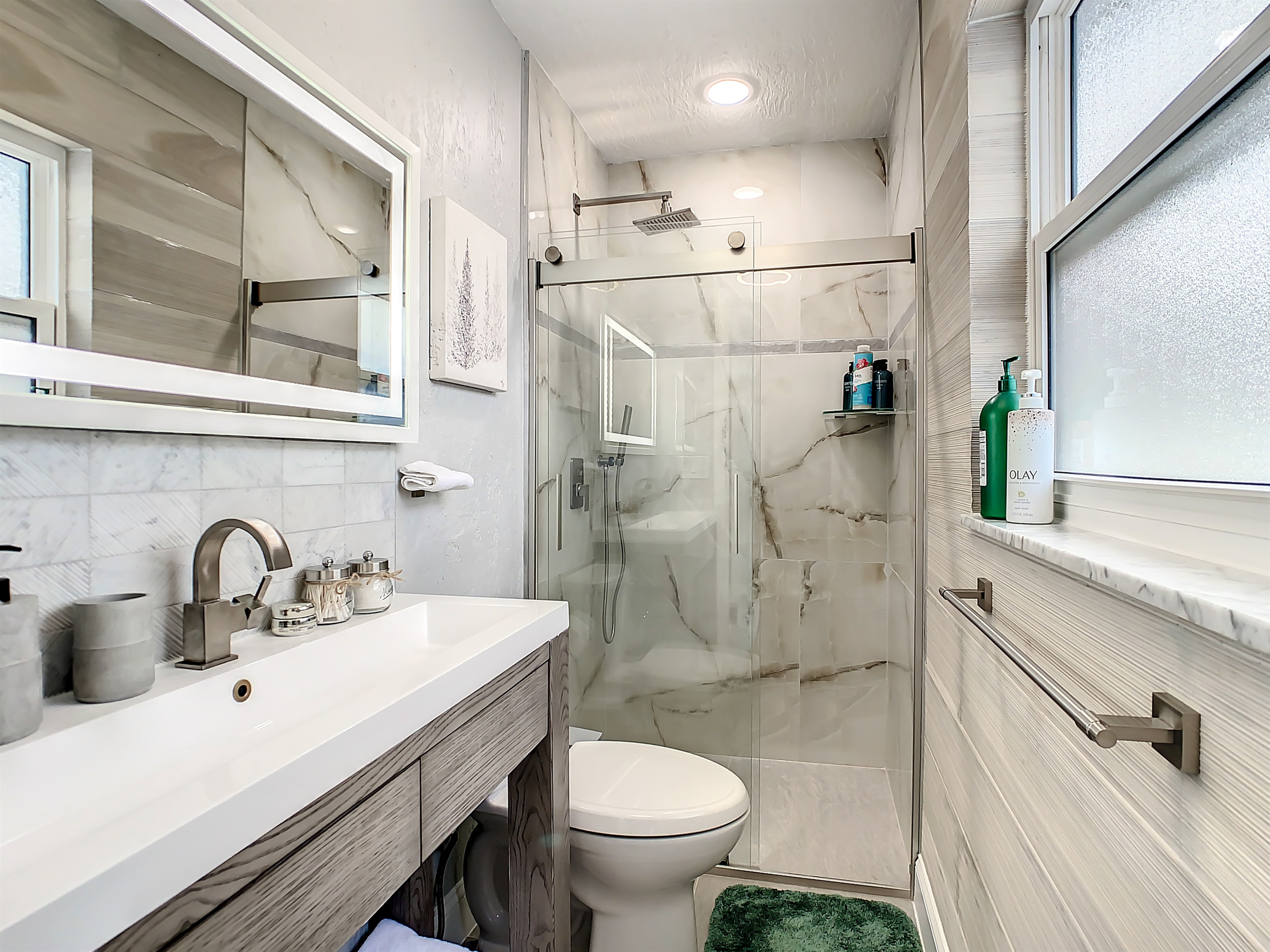 Modern bathroom with glass-enclosed shower, vanity, and large window for natural light.