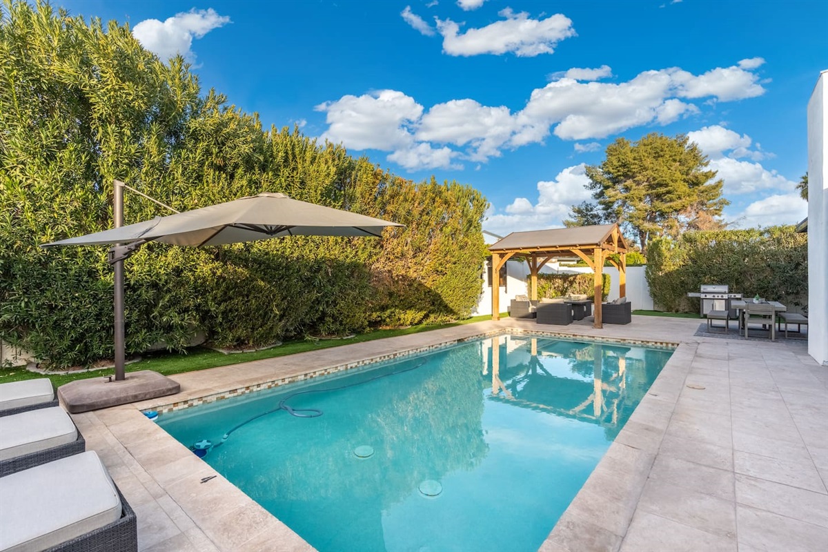 Gaze down the full length of the sparkling pool, showcasing the harmony between shaded relaxation, grilling, and lounging — all within view.