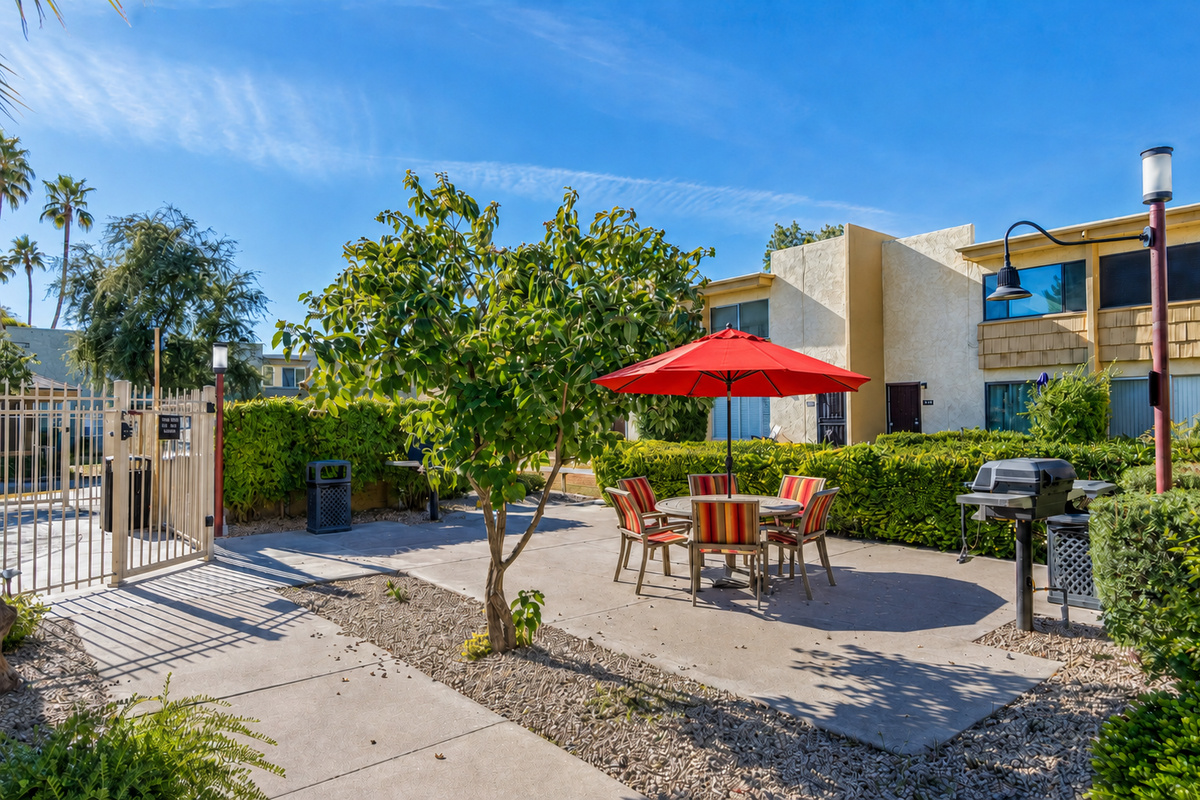 Shared outdoor dining area with a red umbrella, BBQ grill, and pool access nearby.
