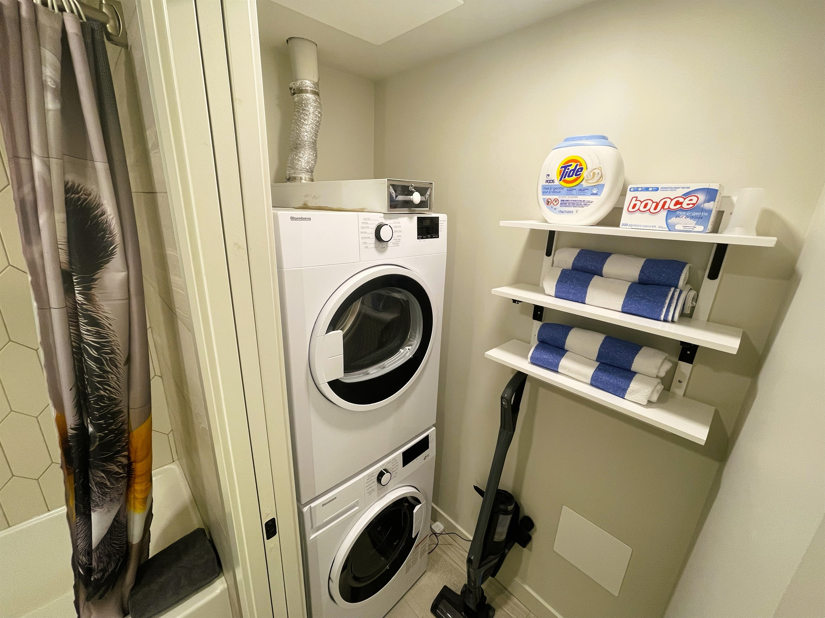 Laundry area next to the bathroom, washer, detergent, dryer, iron, ironing board, cordless vacuum, and pool towels.