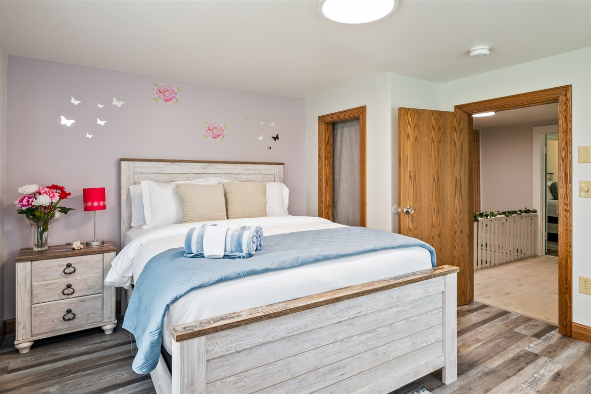 Spacious bedroom with a comfy queen bed, floral accents, and warm natural light—perfect for a restful retreat.