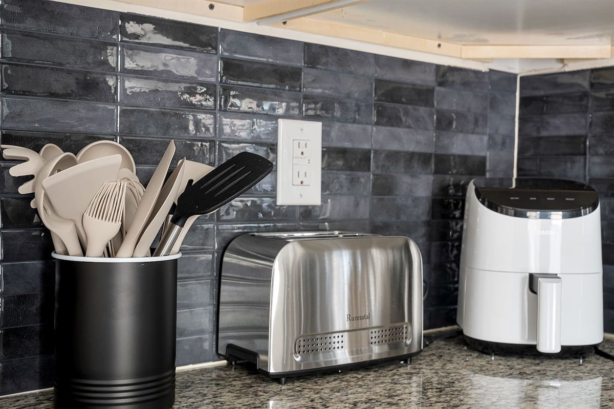 The kitchen is well-equipped with essential appliances, including a toaster and air fryer. The sleek black tile backsplash adds a touch of sophistication.