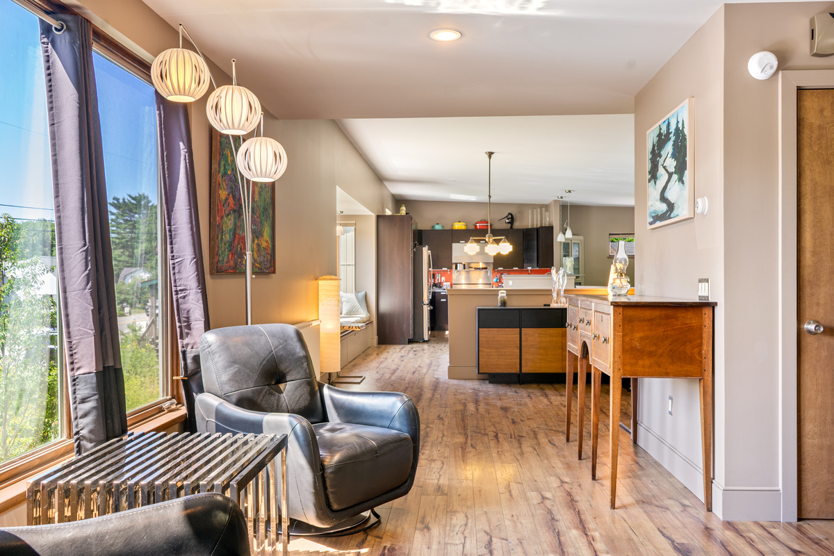 Open-concept living at "The Crag." Relax in plush leather seating beneath modern arc globe lamps, with large view windows illuminating the smooth, flowing layout toward the kitchen, window bench, and dining spaces.