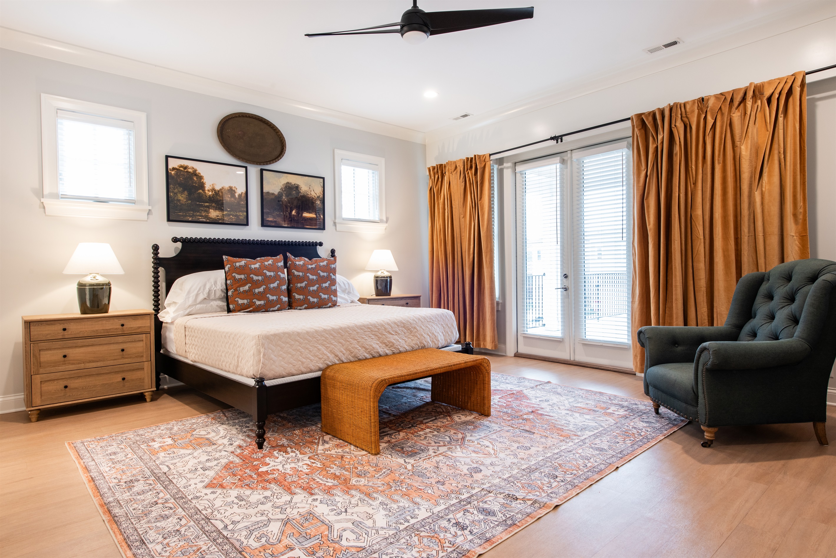 This bedroom combines rustic charm with modern comfort, featuring a king-sized bed with vibrant, bourbon-themed pillows, golden curtains framing & balcony doors.