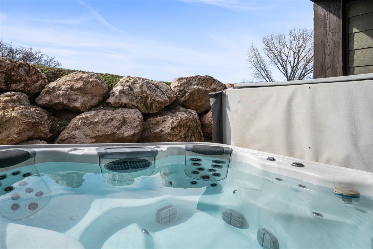 Relax in the private hot tub surrounded by natural rock landscaping for a peaceful retreat.