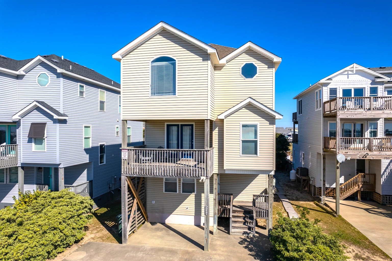 Dawn to Dusk: Front exterior of the home showcasing its elevated coastal design, wide driveway, and spacious three-car parking area.