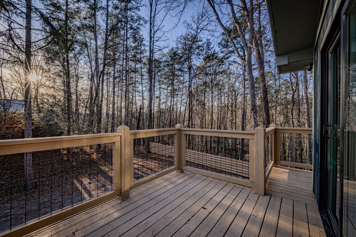 Watch the sun dip below the trees from the glass-railing deck, providing an unobstructed view of the lush mountain landscape.