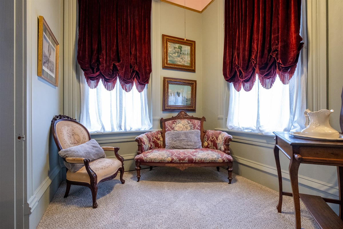 Intimate sitting nook with upholstered seating, natural light, and historic character.