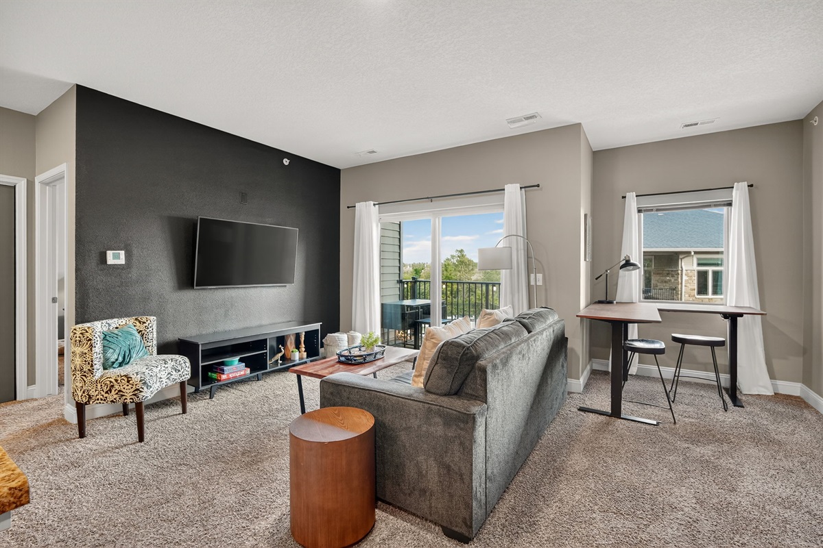 Relax in style with a sleek black accent wall, mounted smart TV, and cozy seating. Natural light pours in from the balcony, creating a perfect balance of comfort and modern design for movie ni