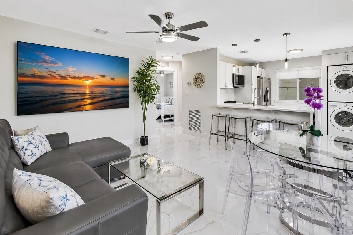 Open-concept living and dining area with a comfortable sectional, 65” Smart TV, dining table, breakfast bar seating, and direct access to the fully equipped kitchen.