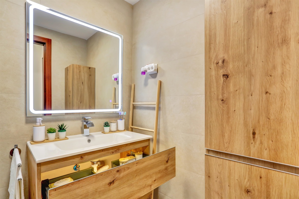 Modern bathroom with a stylish vanity unit, ample storage space, and illuminated mirror, designed for comfort and functionality.