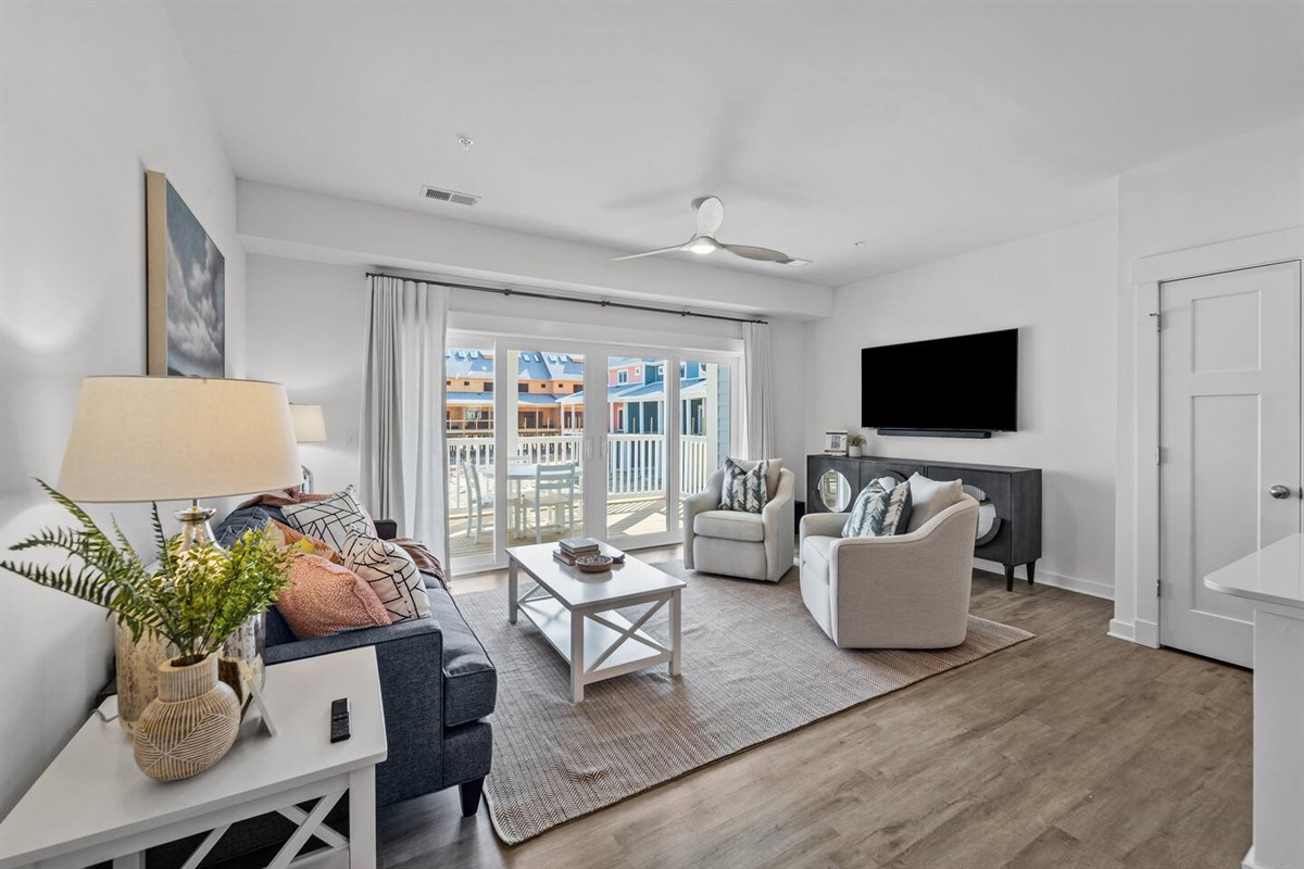 Primary living space with 3-seat couch, 2 swivel chairs, TV, and sliding glass doors to the private patio