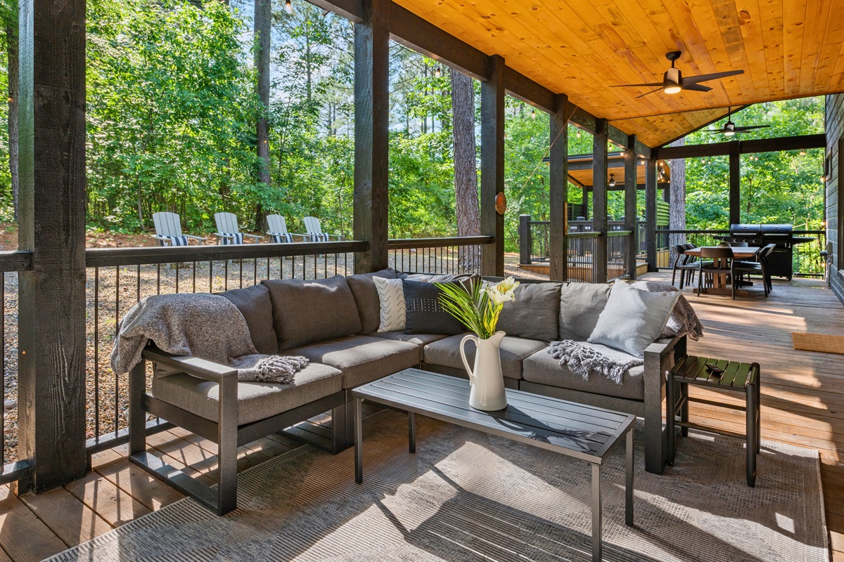 A porch featuring comfortable cushioned seating and a coffee table, with a view of additional outdoor amenities in the background