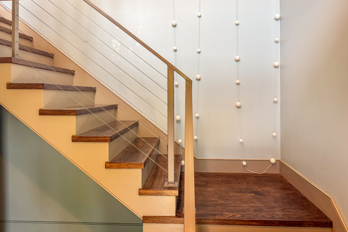 Ascending from Base Camp to the Social Heart. Modern cable railings, rich hardwood treads, and whimsical wall art define "The Crag's" main stairwell, leading guests seamlessly to the central living space and kitchen.