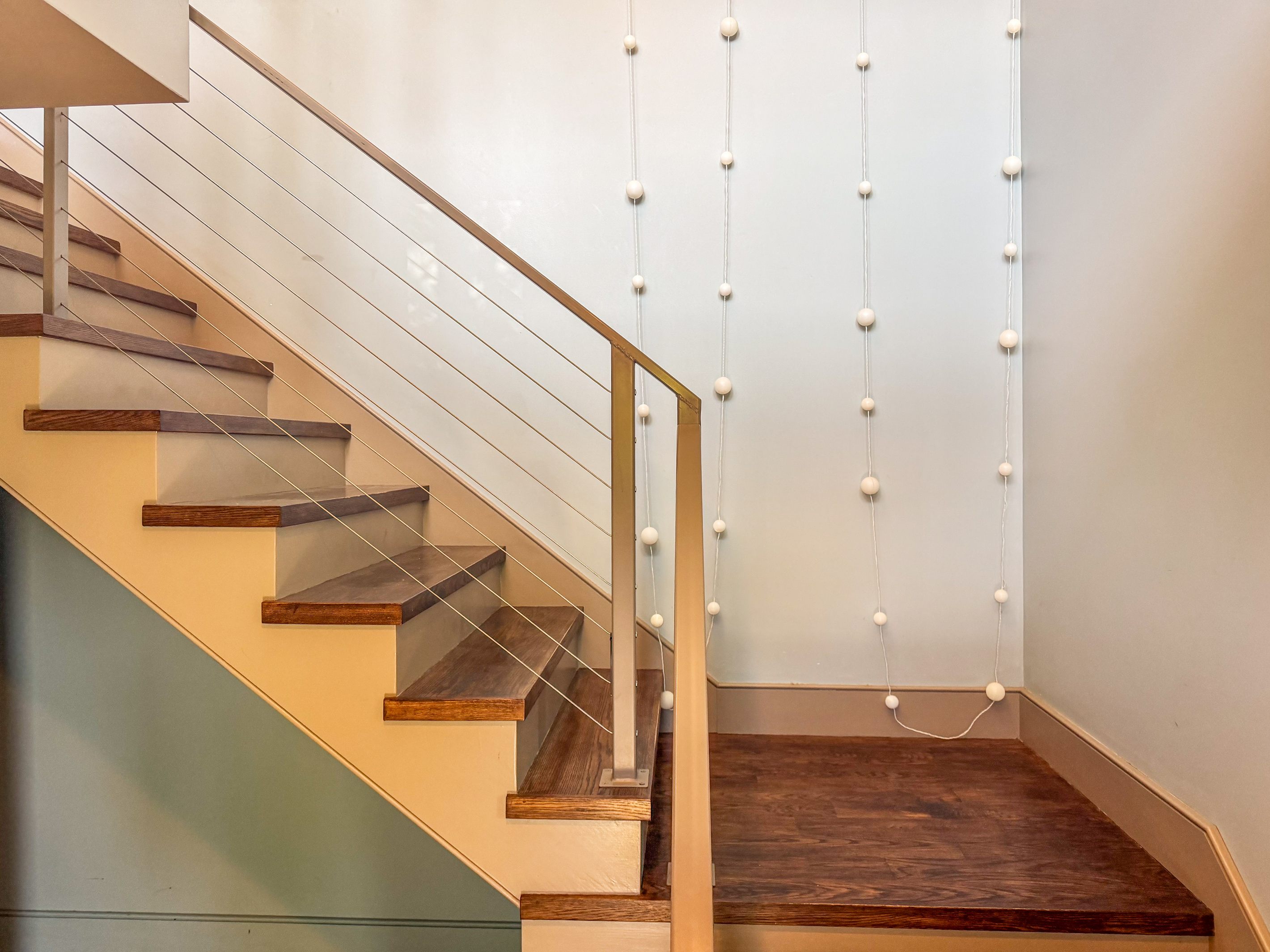 Ascending from Base Camp to the Social Heart. Modern cable railings, rich hardwood treads, and whimsical wall art define "The Crag's" main stairwell, leading guests seamlessly to the central living space and kitchen.