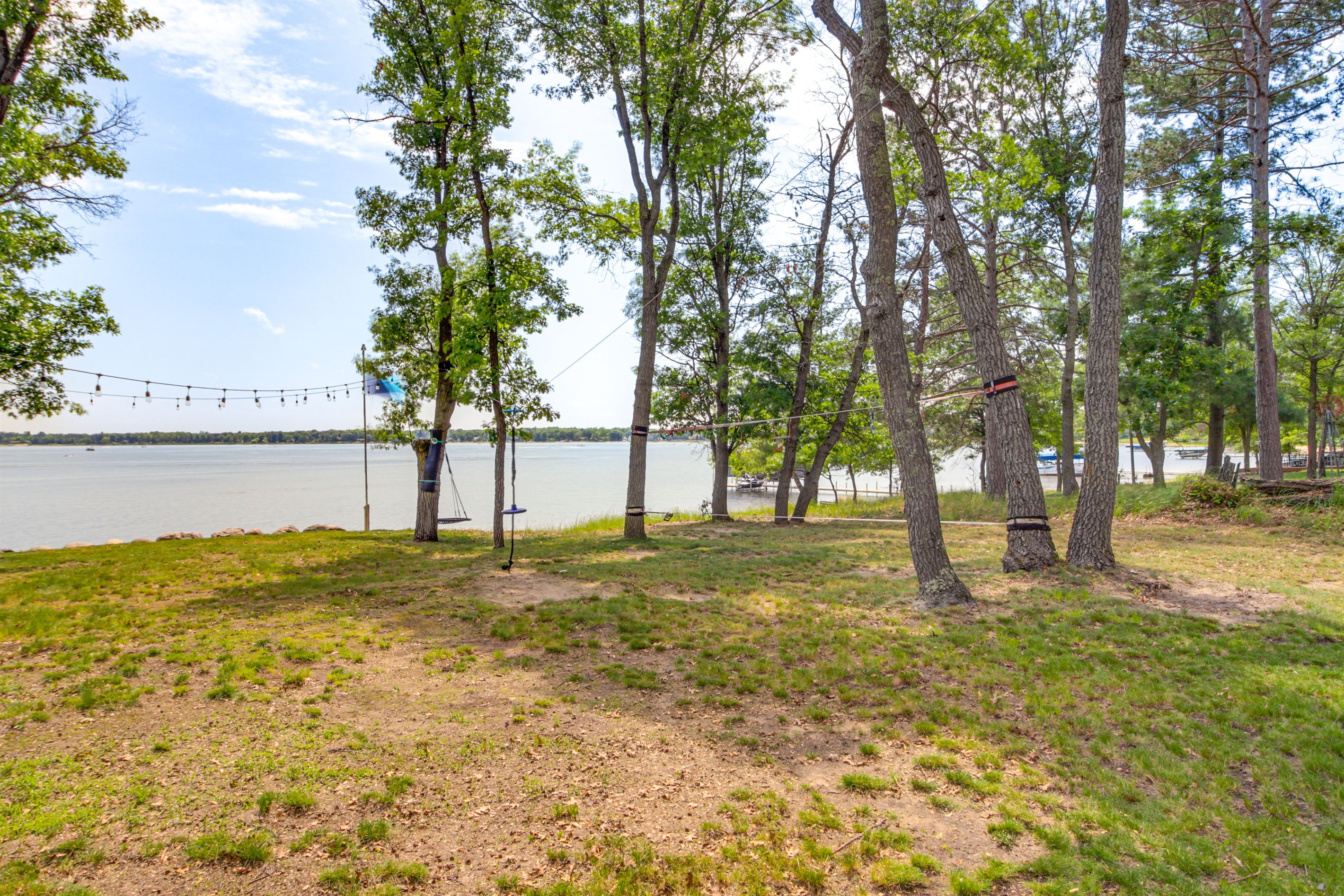 Shaded lakeside yard with mature trees, string lights, and space to relax or play