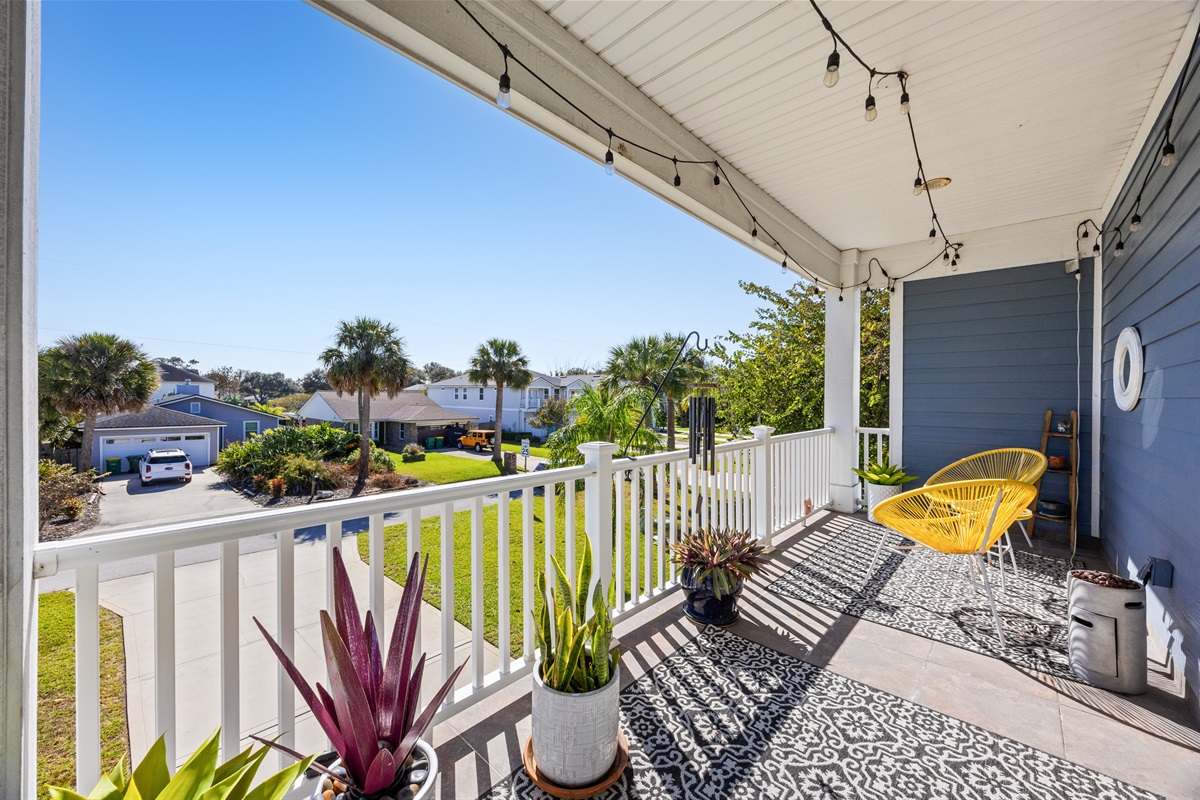 Bright balcony porch (off the primary bedroom) with yellow chairs, potted plants, and string lights in Jacksonville Beach coastal home.