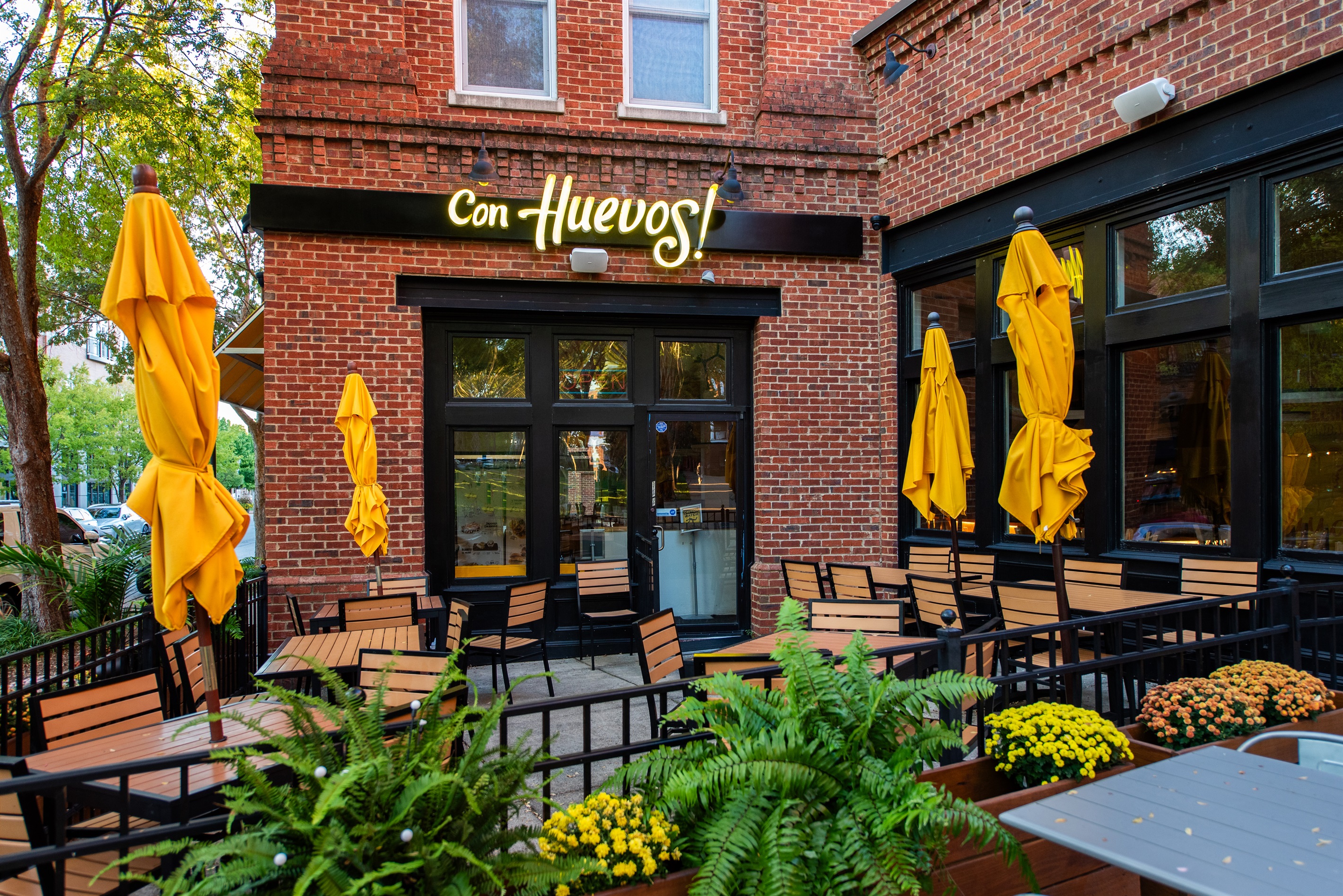 Outdoor patio of "Con Huevos!" in Louisville, KY, with vibrant yellow umbrellas and cozy seating, a 2 minute walk